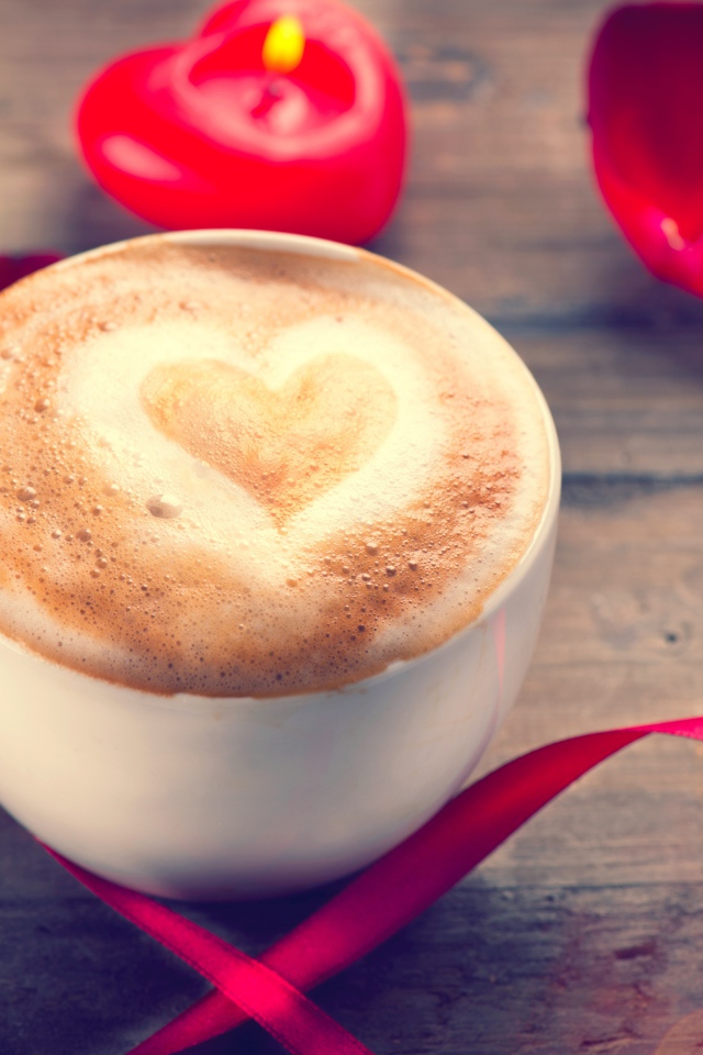 Чашка кофе на столе с красной свечой и лентой