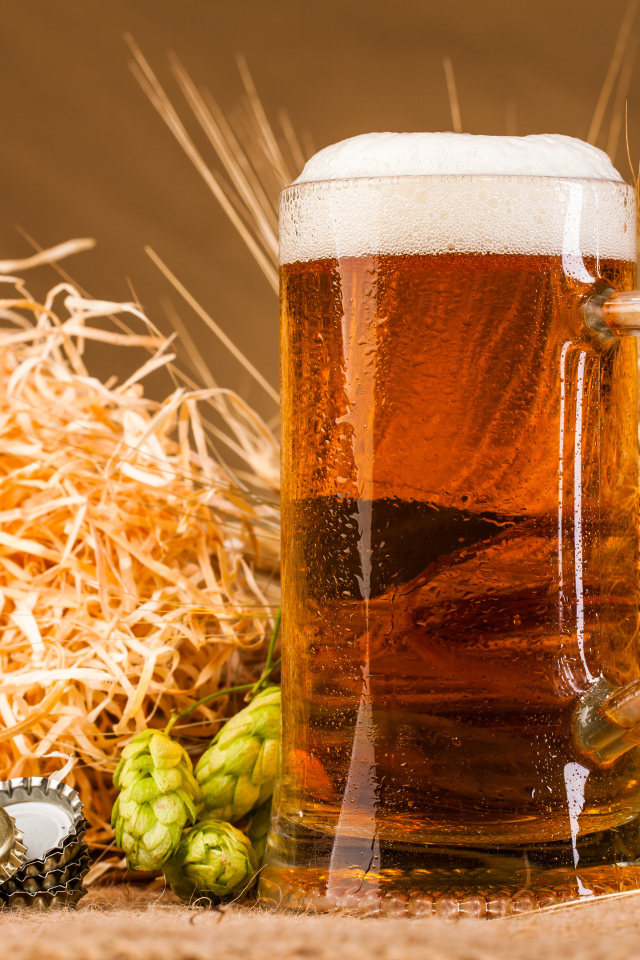 Бокал пива с пеной на столе с хмелем и соломой