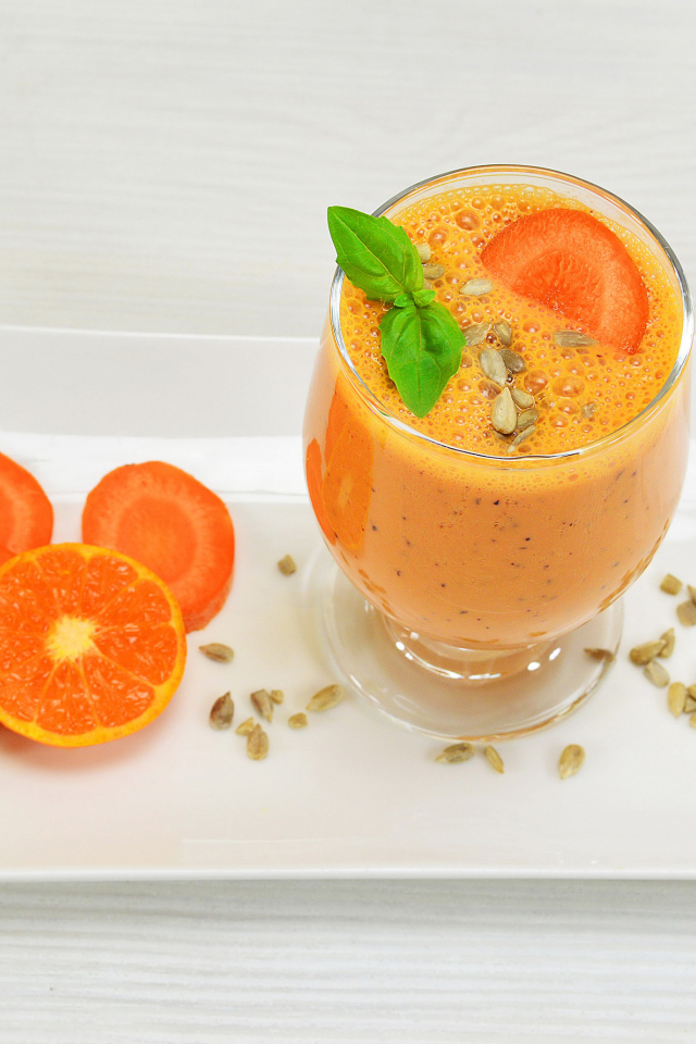 Бокал морковного коктейля с апельсином на белой тарелке