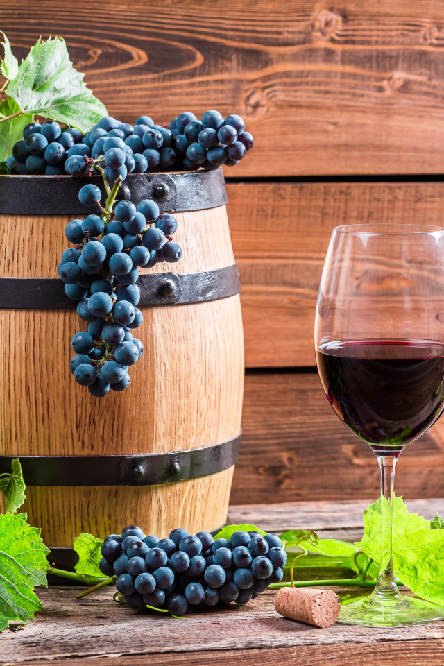 Бокал вина с бочкой и бутылкой на столе с гроздьями синего винограда с листьями