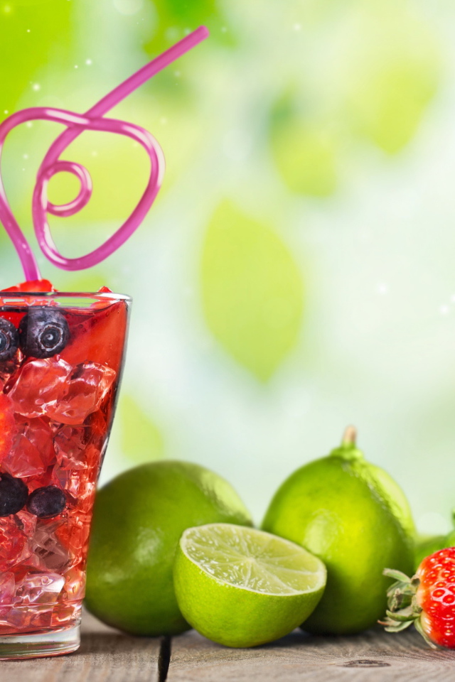 Коктейль с клубникой и ягодами черники в стакане со льдом на столе с лаймами и клубникой