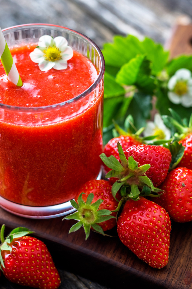 Клубничное смузи с трубочкой и свежими ягодами клубники на разделочной доске