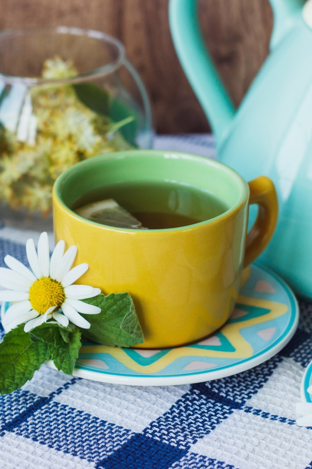 Чай с цветами ромашки в желтой чашке на столе