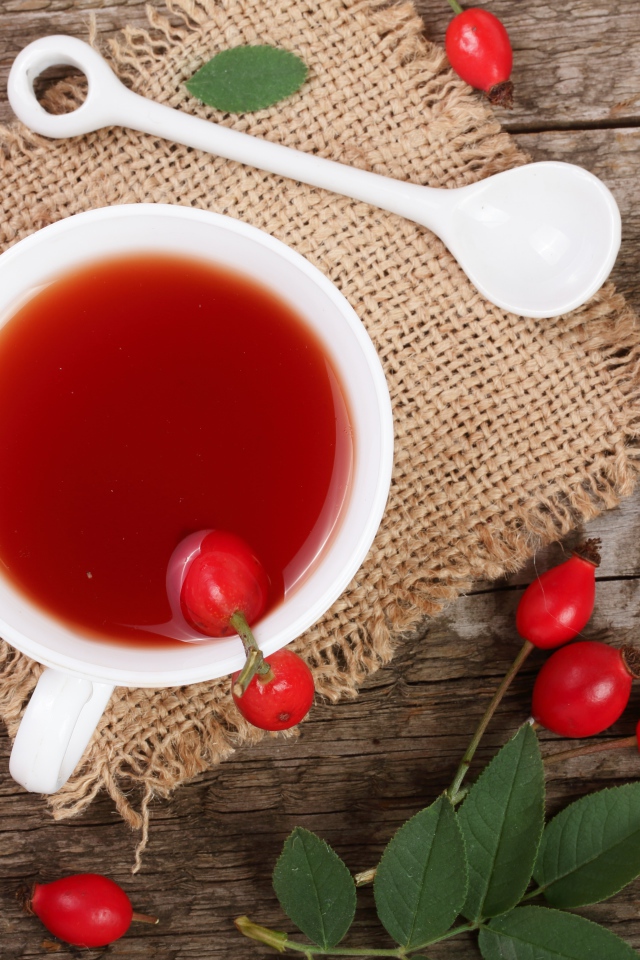 Белая чашка чая с ягодами шиповника на столе