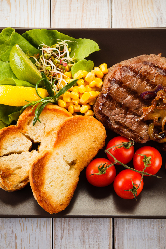 Аппетитный кусок жареного мяса на тарелке с овощами и гренками