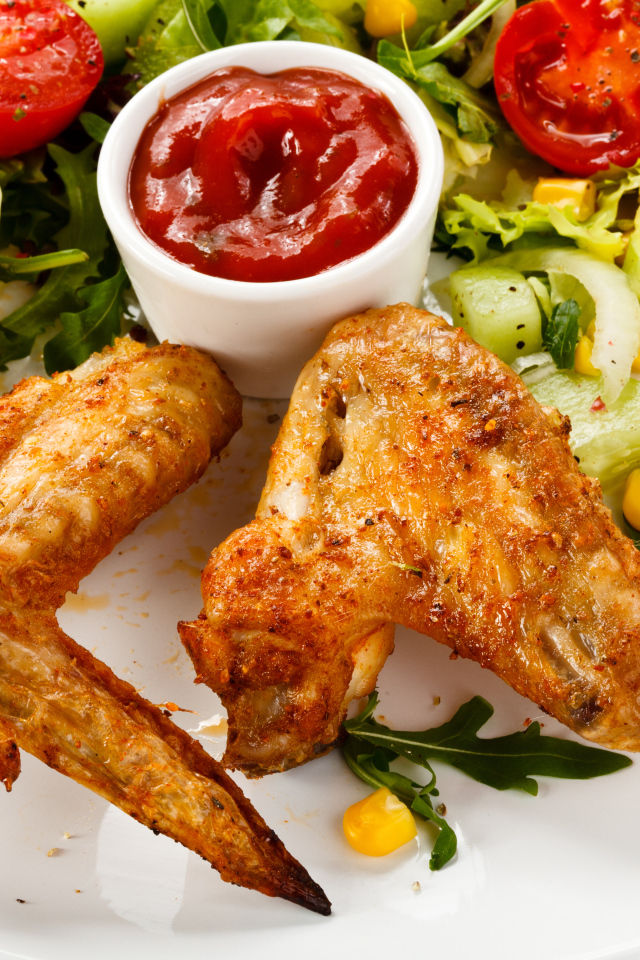Жареные куриные крылышки с овощами и кетчупом на белой тарелке