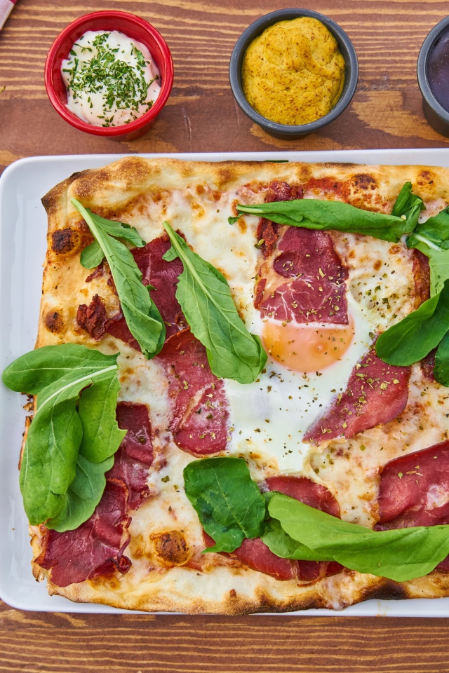 Пицца с беконом и зелеными листьями базилика на столе 