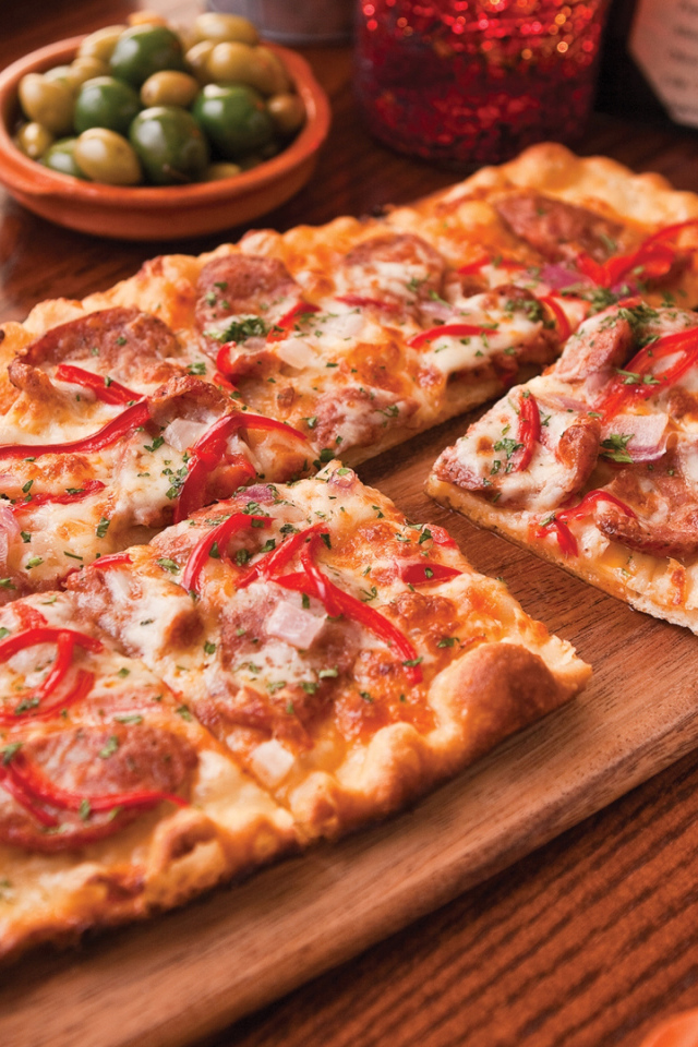 Порезанная на кусочки пицца лежит на разделочной доске