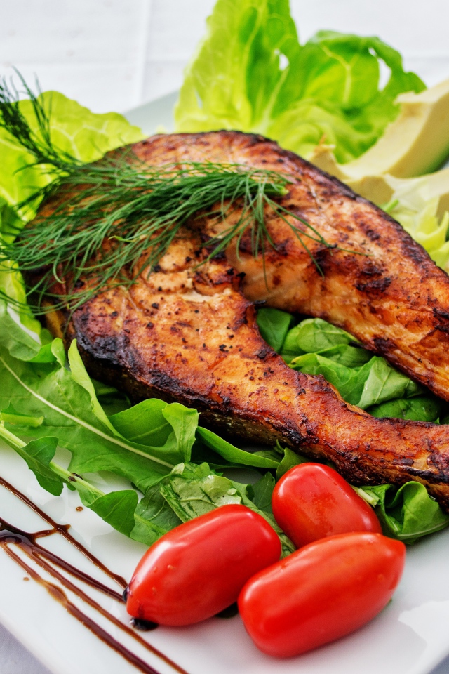 Кусок жареной рыбы на белой тарелке с овощами