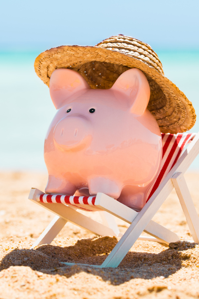 Сувенир свинка в шляпе лежит в игрушечном кресле на пляже