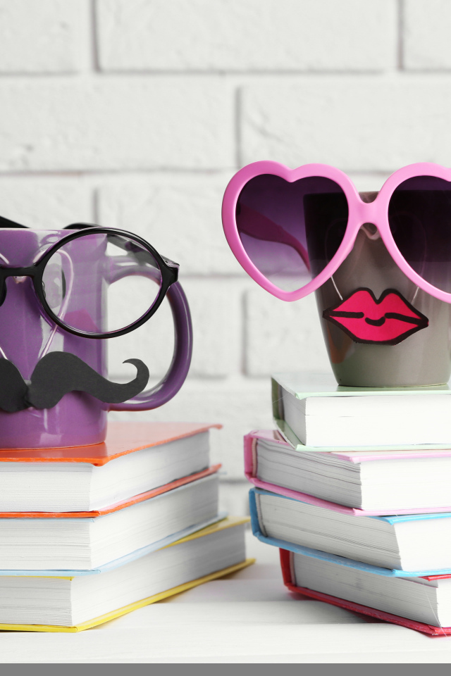 Две забавные чашки в очках стоят на книгах
