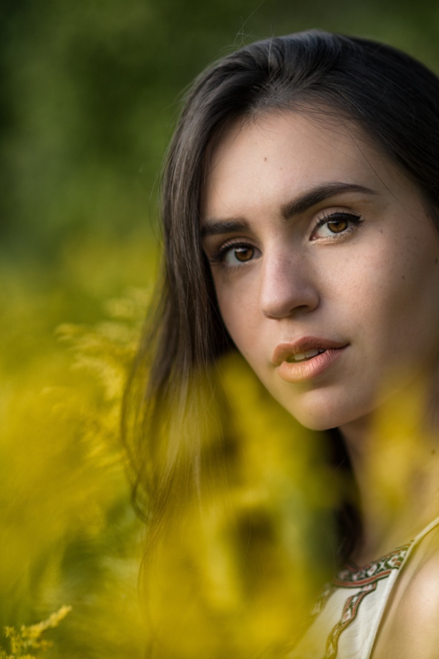 Красивая девушка с нежным взглядом сидит у желтых цветов