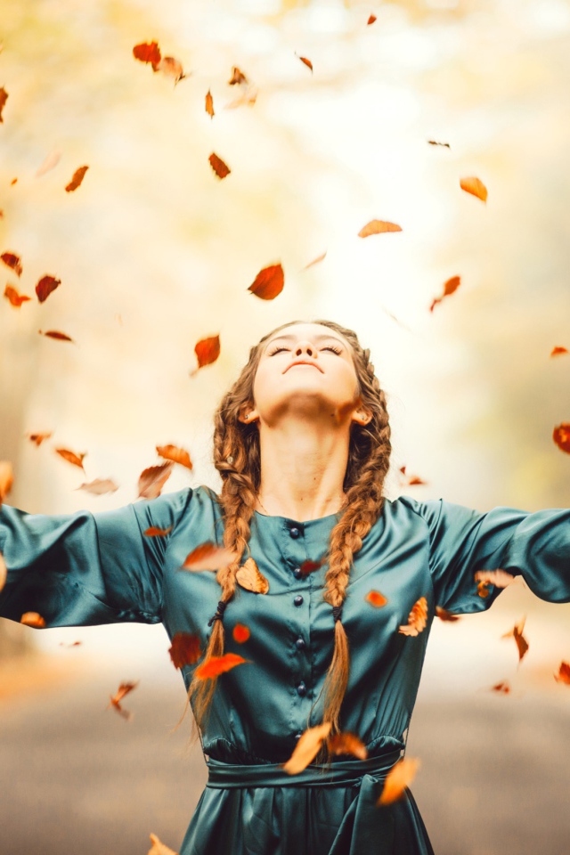 Красивая девушка с косичками подбрасывает желтые листья осенью