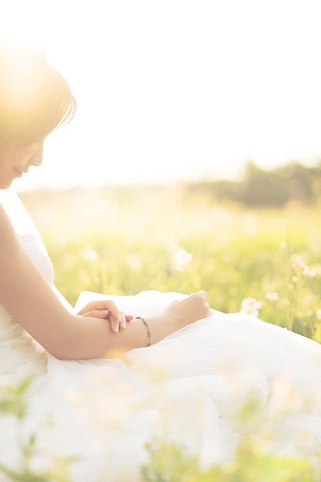 Девушка азиатка в платье невесты сидит на траве в поле 