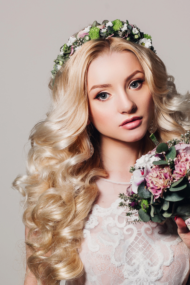 Красивая блондинка в свадебном платье с букетом цветов на сером фоне