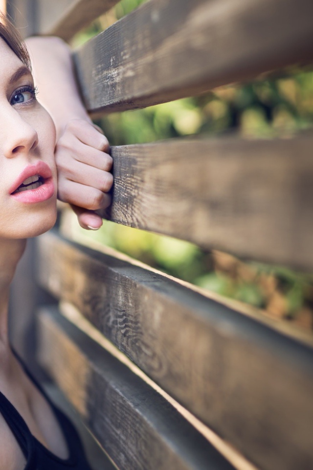 Красивая голубоглазая девушка у деревянного забора 