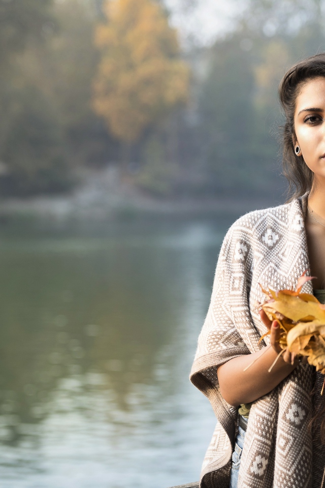 Красивая брюнетка у реки с желтыми листьями в руках