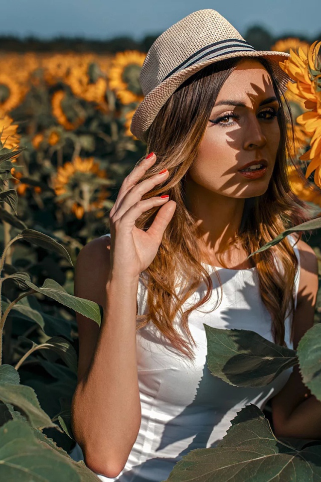 Красивая девушка в шляпе стоит на поле с подсолнухами