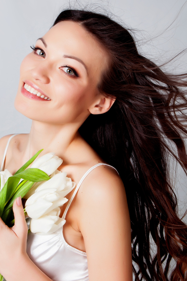 Красивая улыбающаяся брюнетка с букетом тюльпанов на сером фоне