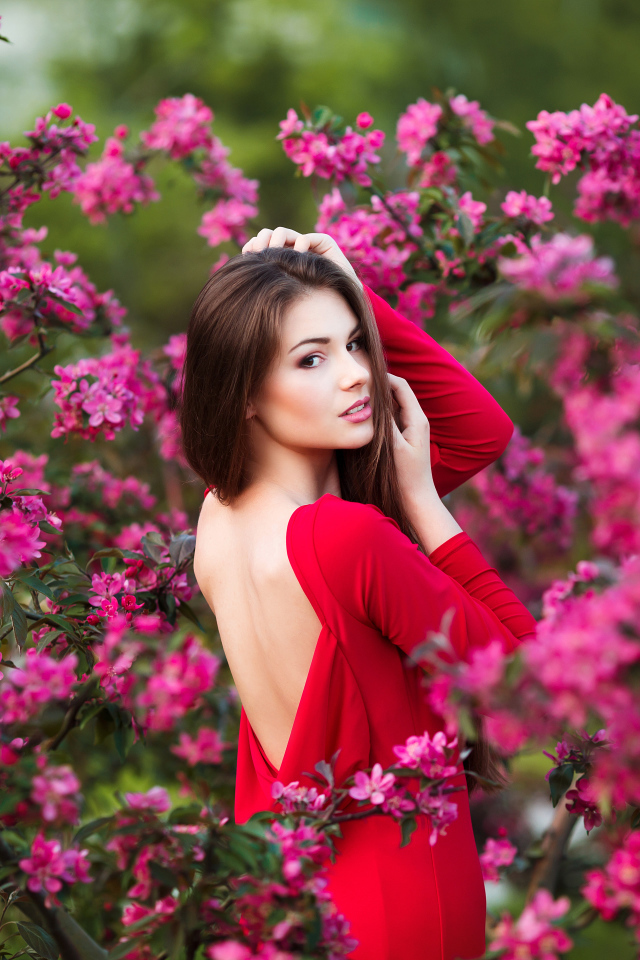 Красивая молодая девушка в красном платье на фоне розовых цветов