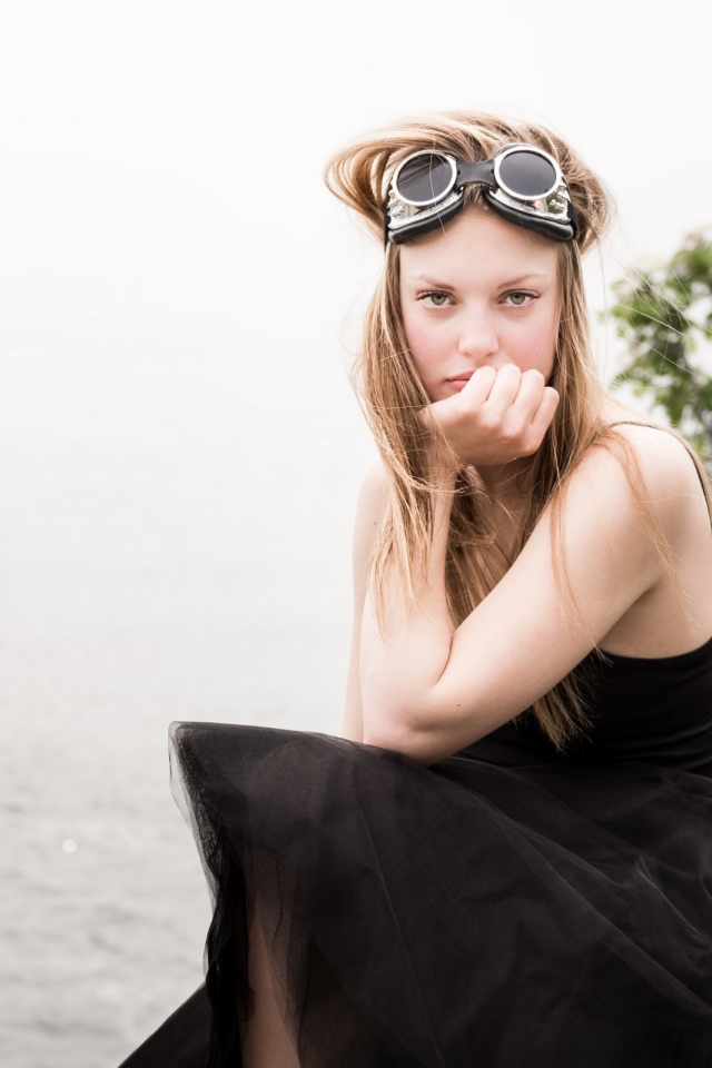 Девушка блондинка с очками на голове сидит на камне