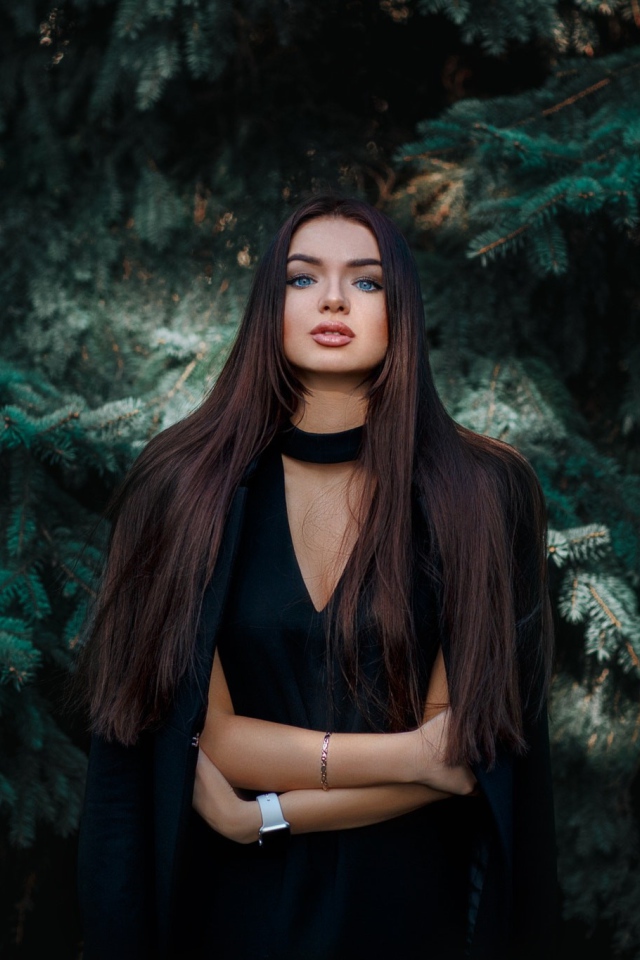 Голубоглазая девушка брюнетка у большой зеленой ели 