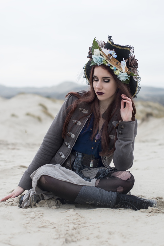 Девушка брюнетка  в костюме сидит на песке 