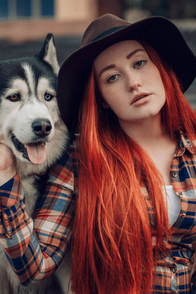 Рыжеволосая девушка в черной шляпе сидит с хаски