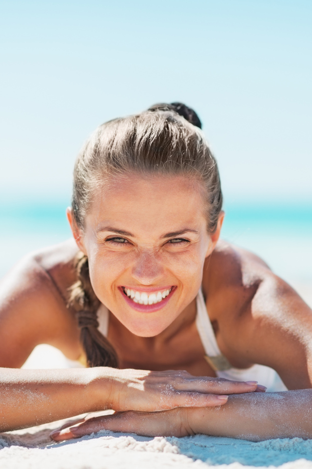 Улыбающаяся девушка лежит на белом песке на пляже