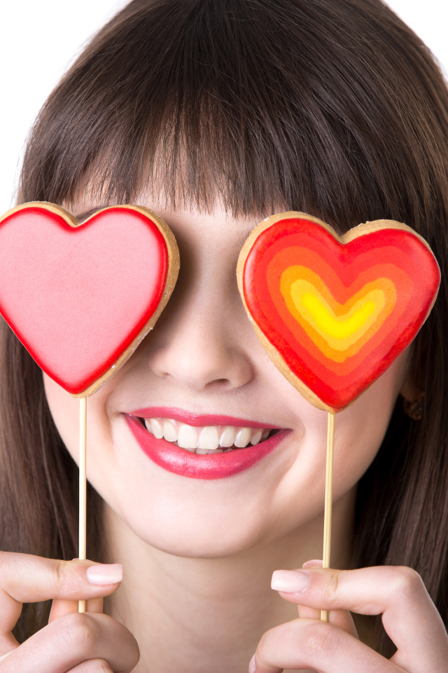 Красивая девушка шатенка закрыла глаза леденцами в форме сердца