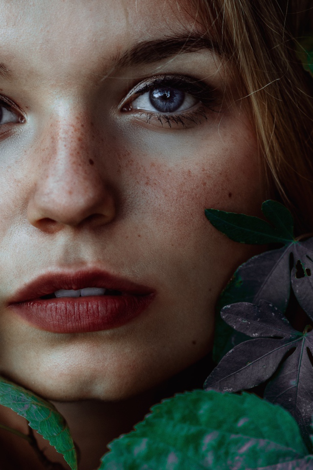 Лицо красивой голубоглазой девушки украшено зелеными листьями