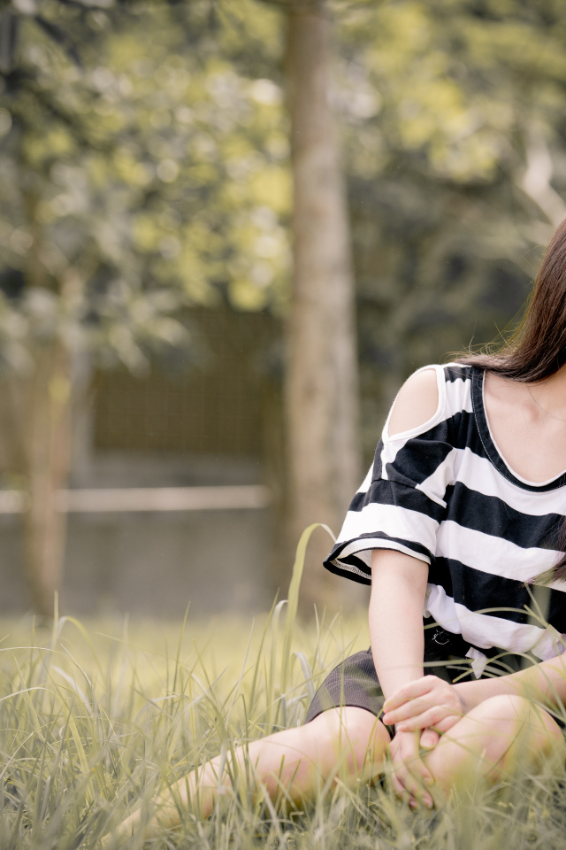 Молодая девушка азиатка сидит на траве у дерева