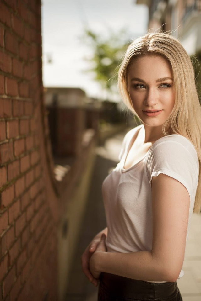 Молодая девушка блондинка у кирпичной стены 