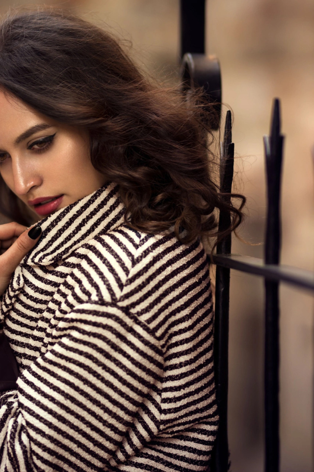 Молодая брюнетка в пальто у забора