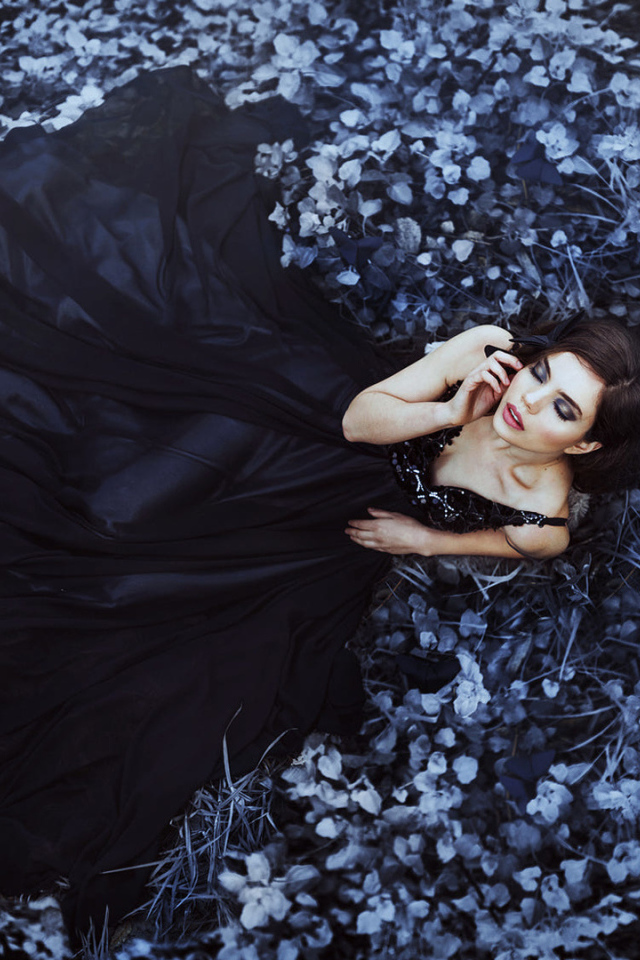 Молодая девушка модель с красивом черном платье лежит на траве