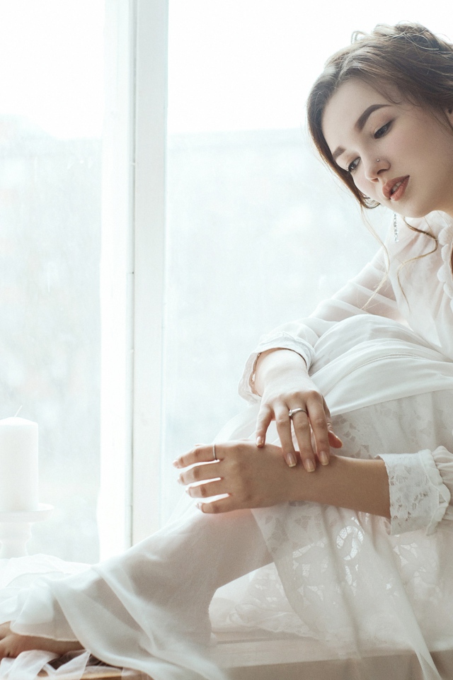 Молодая грустная девушка в белом платье у окна