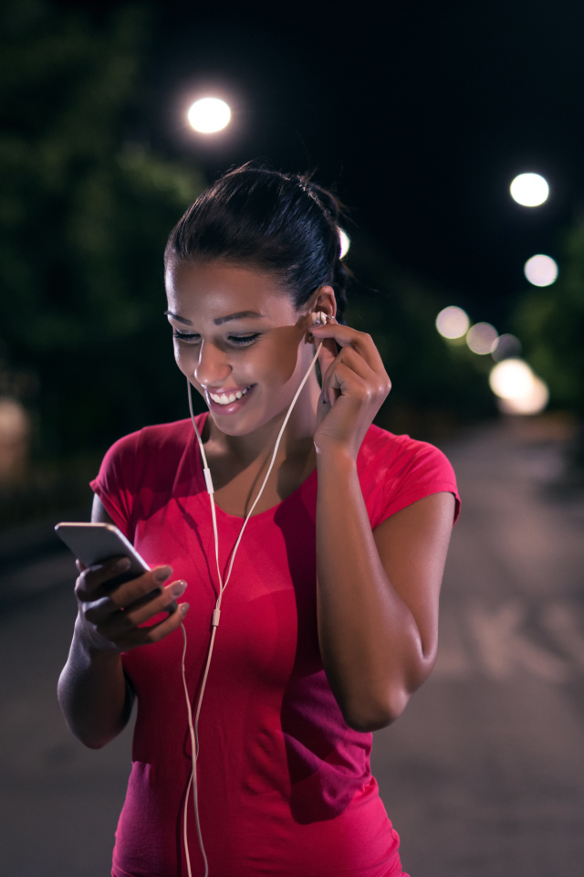 Молодая улыбающаяся девушка в наушниках с телефоном в руках