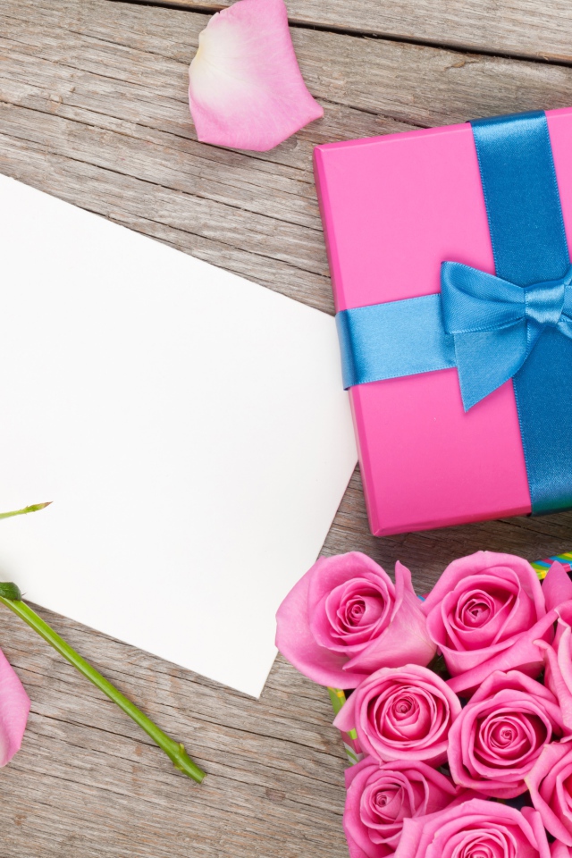 Box with a gift on the table with a bouquet of pink roses and a sheet of paper