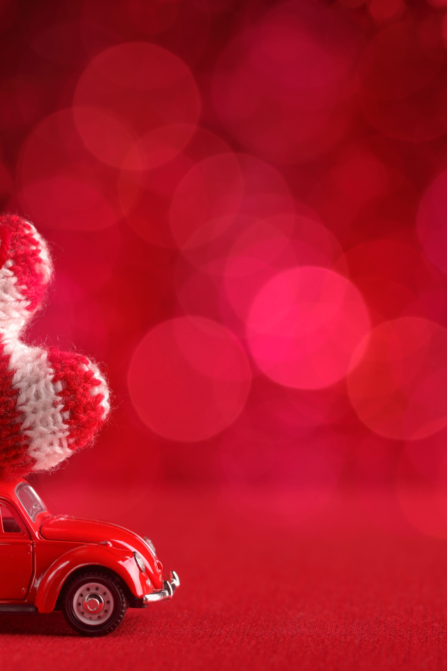 Красная игрушечная машинка везет с сердечко на розовом фоне, фон для открытки на День Святого Валентина