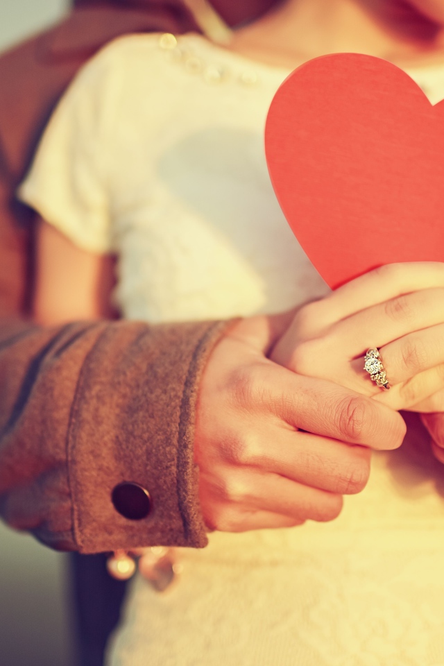 Влюбленная пара держит в руках красное бумажное сердце