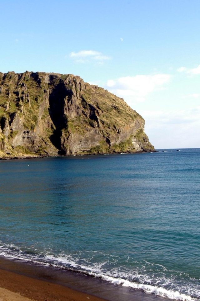 Гора на фоне спокойной воды моря под голубым небом