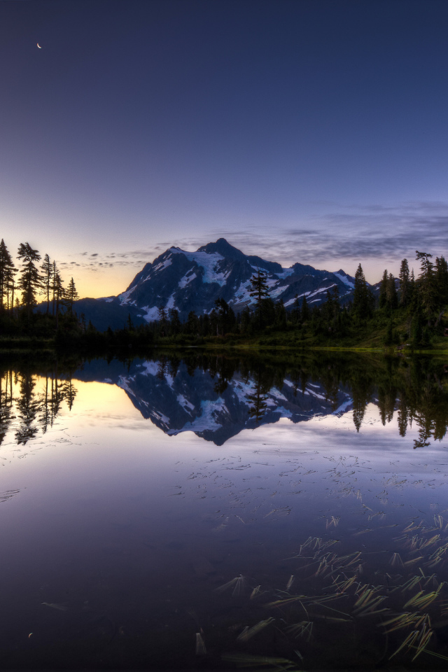 Заснеженная гора и лес отражается в озере вечером
