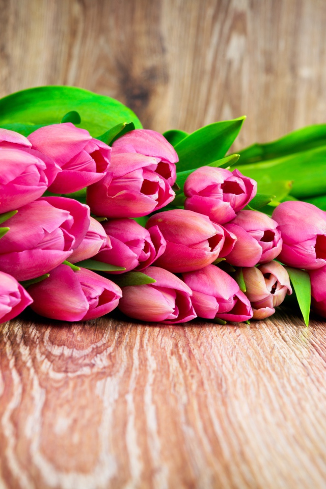 Букет розовых тюльпанов лежит на деревянной поверхности
