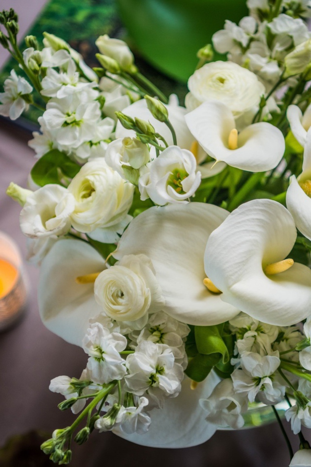 Букет белых цветов зантедеския и левкой с зажженными свечами на столе