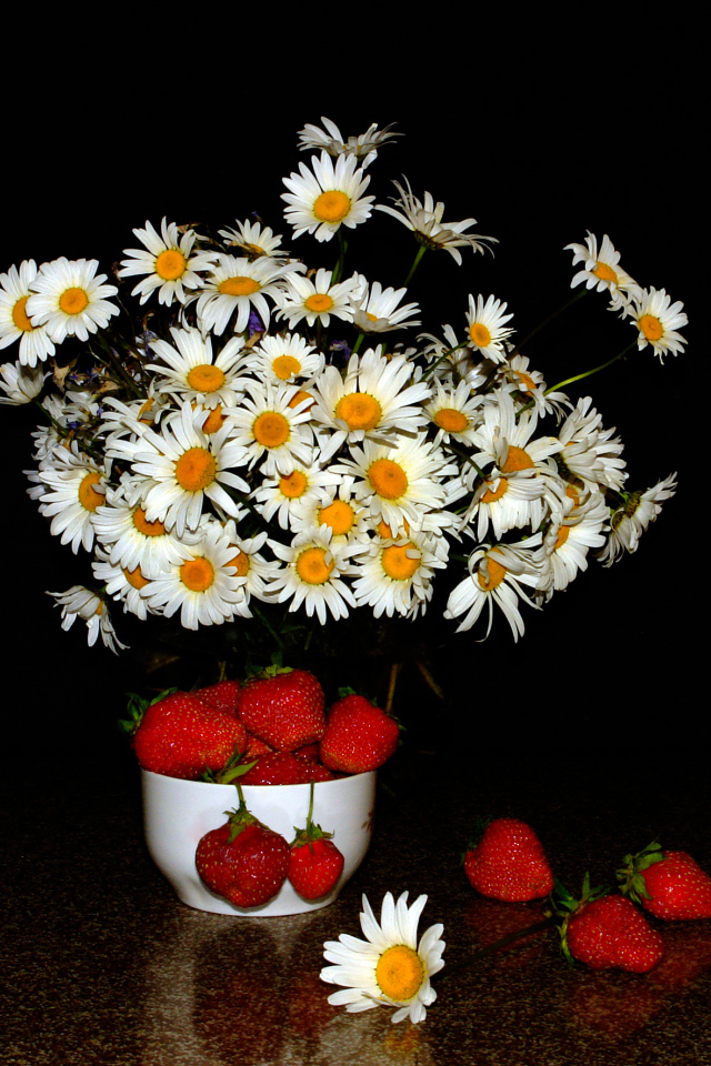 Белые полевые ромашки и клубника на столе на черном фоне