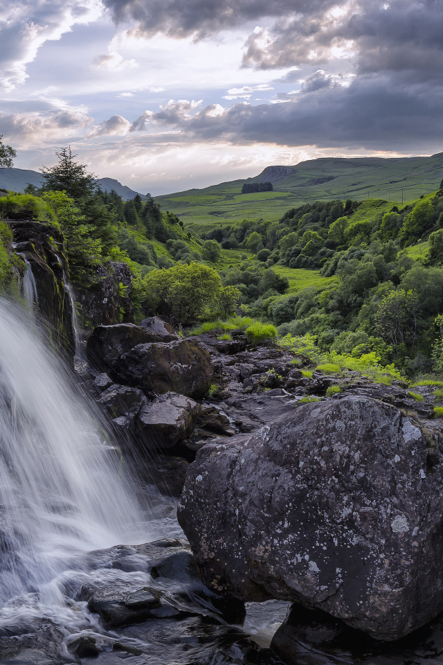 Водопад стекает по камням на фоне красивого неба и зеленого леса