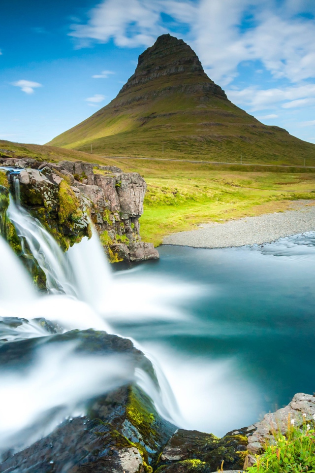Водопад стекает в реку на фоне горы под красивым небом