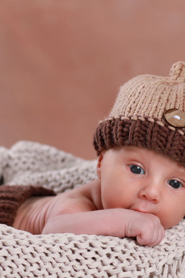 Грудной ребенок лежит в вязаной коричневой шапке