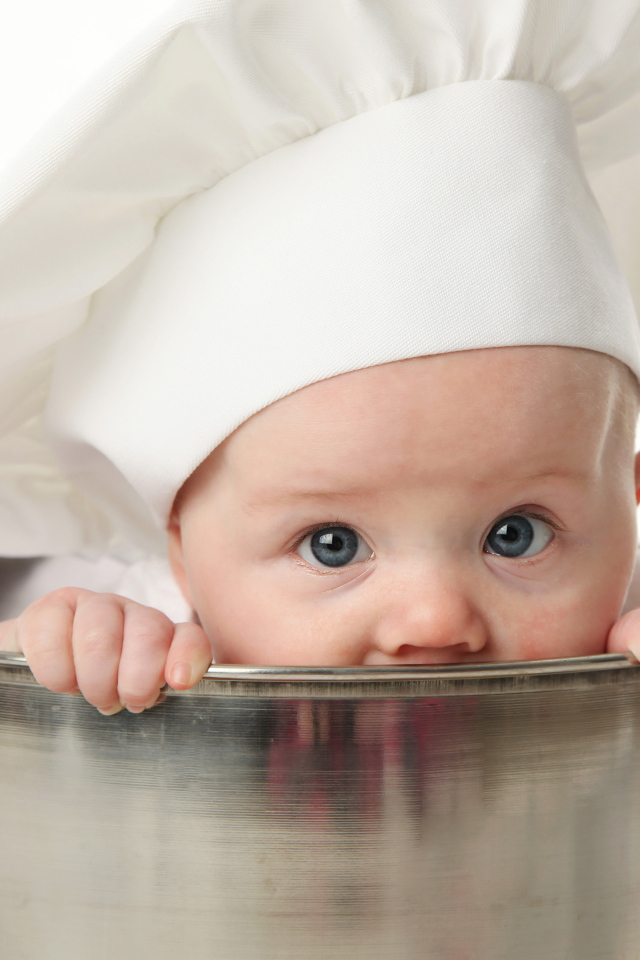 Грудной ребенок в шапке повара сидит в большой кастрюле