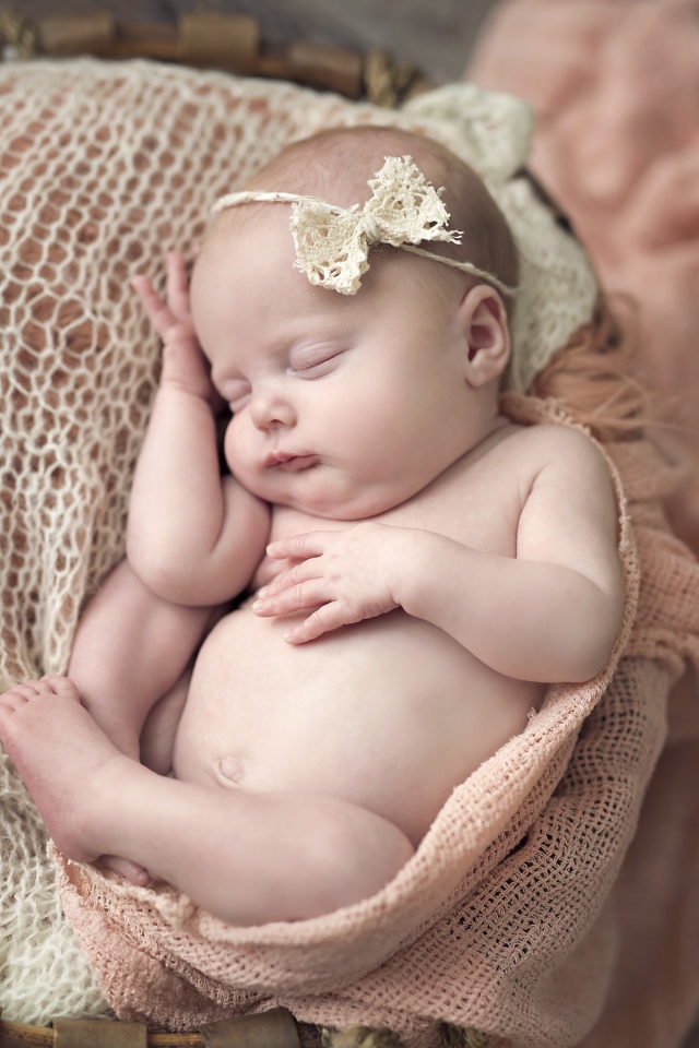 Грудной ребенок с бантиком на голове спит в корзине